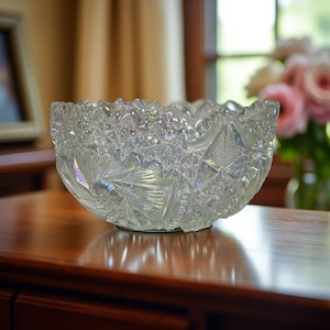 May include: Clear, iridescent glass bowl with a starburst pattern. The bowl has a scalloped rim and sits on a wooden surface. The bowl is likely vintage and suitable for serving or display.
