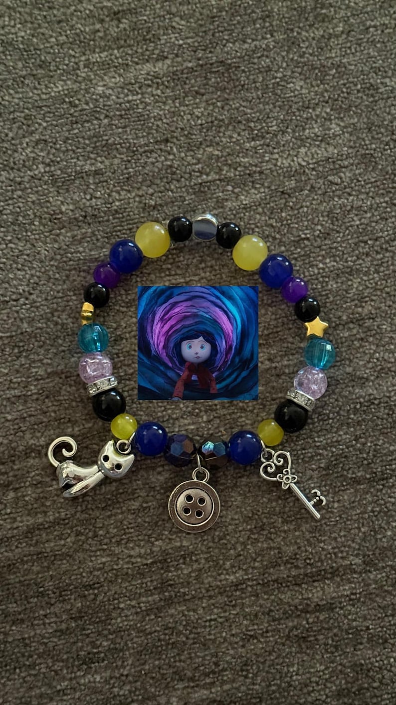 May include: A beaded bracelet featuring a central image of a girl in a tunnel. The bracelet includes charms of a cat, a key, and a button. Beads are in various colors including blue, yellow, purple, and black.