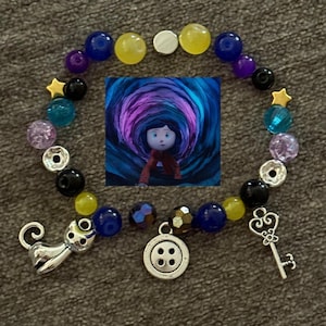 May include: A beaded bracelet featuring a central image of a character in a tunnel. The bracelet includes blue, yellow, purple, and clear beads, along with charms of a cat, a key, and a button. The bracelet is designed with a variety of colors and shapes.