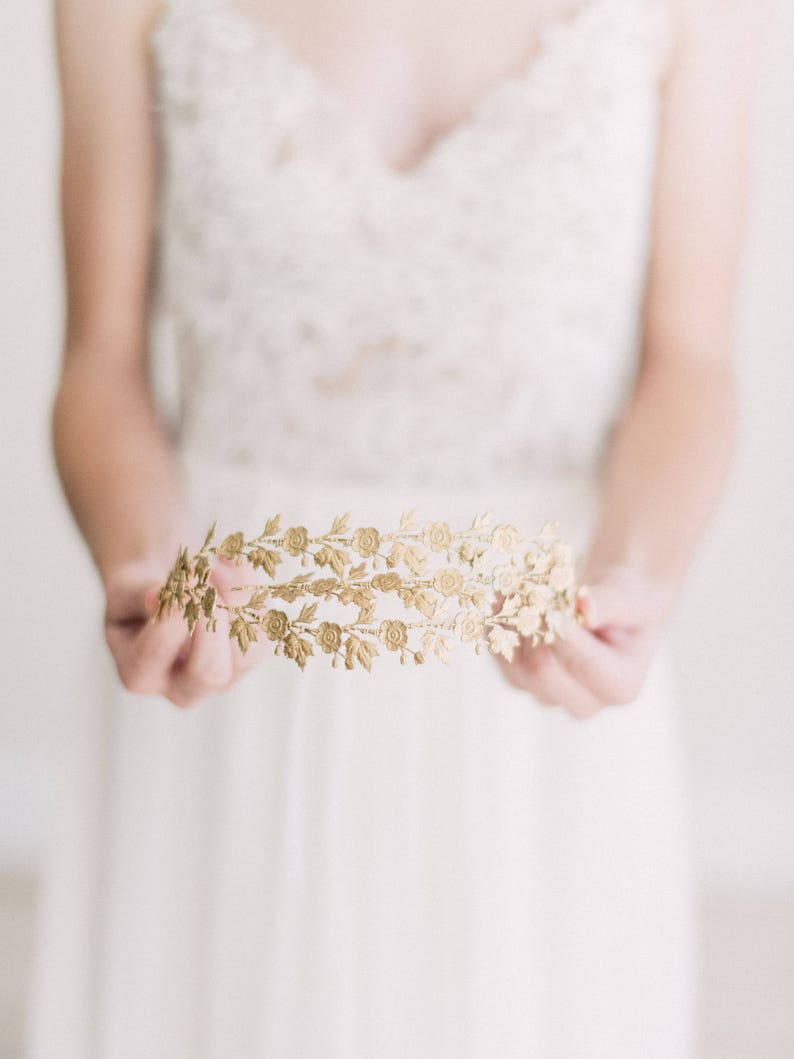 May include: A gold floral crown with delicate leaves and small roses. The crown is made of metal and has a delicate, feminine design.