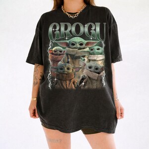 May include: Black t-shirt featuring a graphic of Grogu, also known as Baby Yoda, from The Mandalorian. The design includes multiple images of Grogu with the word "GROGU" in a green, retro-style font. The shirt has a vintage, worn look.