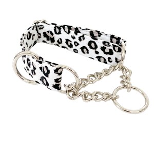 Puede incluir: Un collar de perro de estampado de leopardo blanco y negro con una cadena plateada y dos anillos plateados.