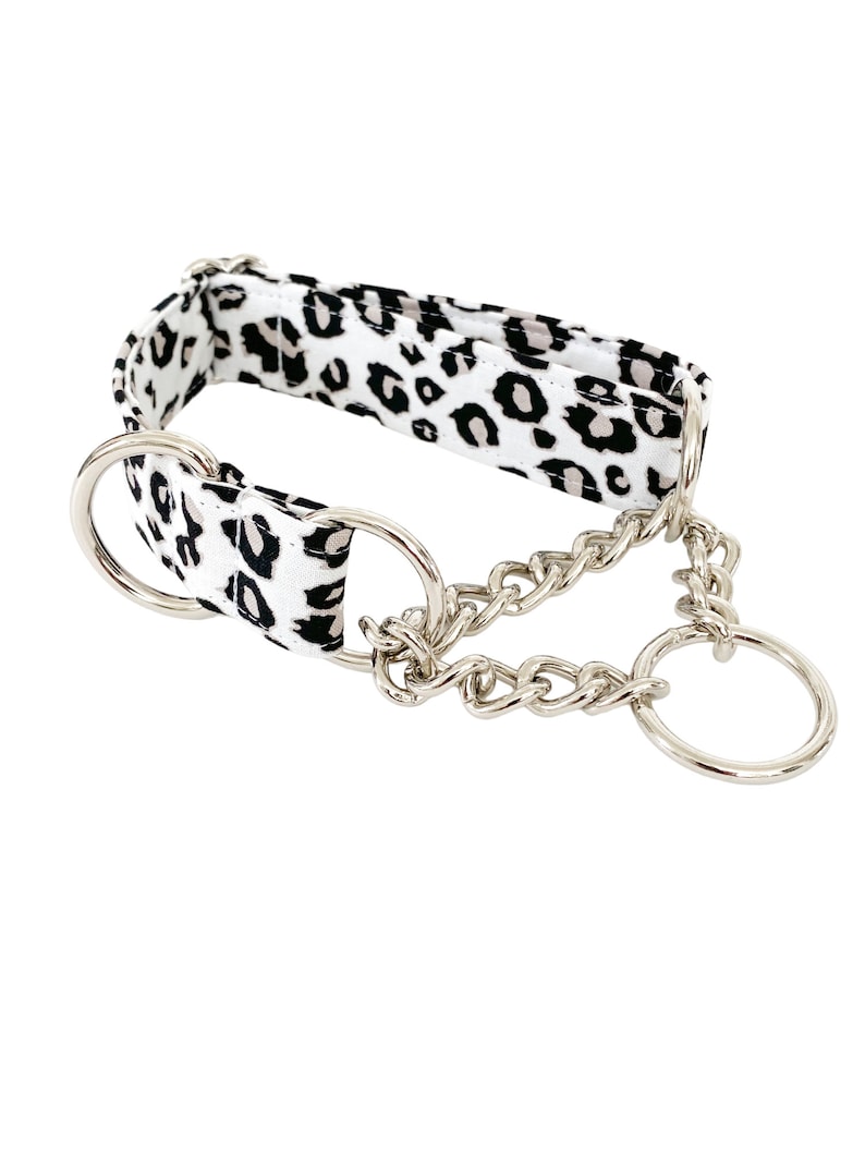 Puede incluir: Un collar de perro de estampado de leopardo blanco y negro con una cadena plateada y dos anillos plateados.