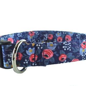 May include: A navy blue dog collar with a floral pattern featuring pink and blue flowers. The collar has a black plastic buckle and a silver metal D-ring.