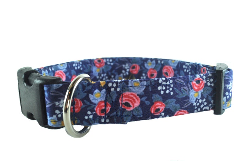 May include: A navy blue dog collar with a floral pattern featuring pink and blue flowers. The collar has a black plastic buckle and a silver metal D-ring.