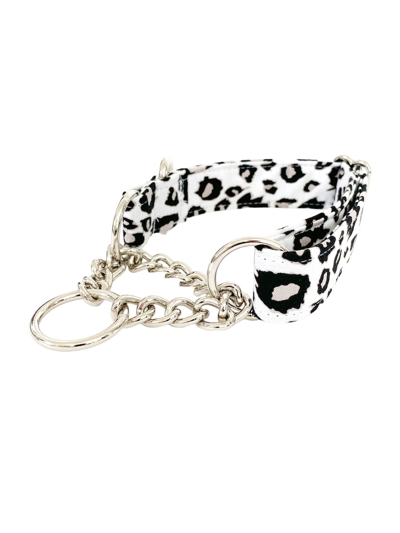 Puede incluir: Un collar de perro de estampado de leopardo blanco y negro con una cadena plateada y dos anillos plateados.
