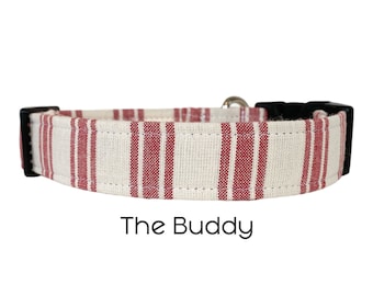 Puede incluir: Un collar de perro a rayas blancas y rojas con una hebilla negra. El collar tiene el texto "The Buddy" impreso debajo.