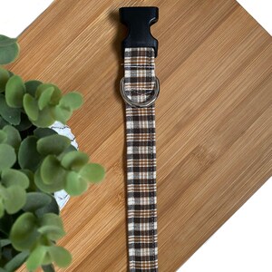 May include: A brown and beige plaid dog collar with a black plastic buckle and a silver metal D-ring.