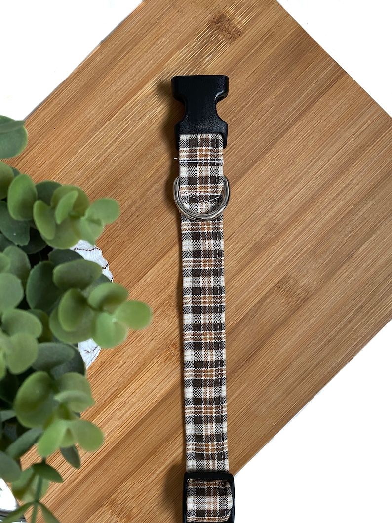 May include: A brown and beige plaid dog collar with a black plastic buckle and a silver metal D-ring.