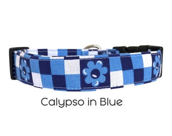 Op de afbeelding: Hondenhalsband met een blauw-wit ruitpatroon en bloemmotieven. Het heeft een zwarte plastic gesp en een zilveren metalen lus. De tekst "Calypso in Blue" staat eronder.
