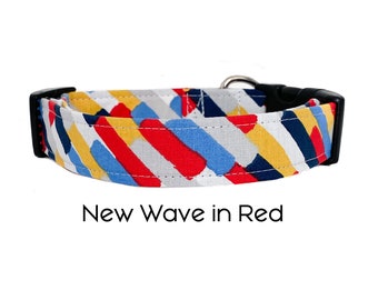 Puede incluir: Un collar de perro blanco con un patrón geométrico en rojo, amarillo, azul y negro. El collar tiene una hebilla negra y un anillo en D plateado. El texto "New Wave in Red" está impreso debajo del collar.