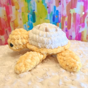 May include: A crocheted yellow and white plush turtle toy. The turtle has a soft, fuzzy texture and a detailed shell.