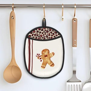 May include: A kitchen scene featuring a gingerbread man pot holder with a leopard print top, hanging from a gold rod. Wooden spoon, spatulas, and a ladle hang nearby. Clear jars and a container with food are on the counter below.