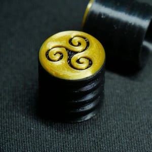 May include: A black and gold bottle stopper featuring a spiral design. The top is gold with a three-part spiral pattern. The base is black and cylindrical. The stopper is likely made of plastic.