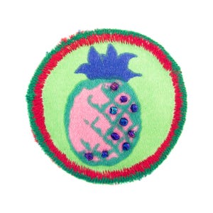 Könnte beinhalten: Runder, gestickter Aufnäher mit einem rosa Ananas-Design und blauen und violetten Akzenten. Die Ananas befindet sich auf einem hellgrünen Hintergrund, umrandet von einem rot-grünen Rand. Kleine Perlen sind auf die Ananas genäht.