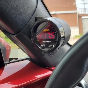 May include: A black gauge with a red digital display reading "4.75" and the text "TRU-BOOSTX". The gauge is mounted in a car's interior.
