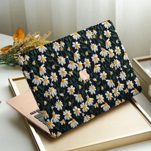 May include: A black laptop case with a daisy floral pattern. The case features white daisies with yellow centers and green stems and leaves. The laptop is gold in color.