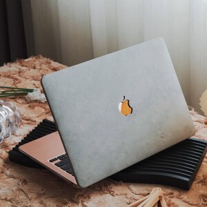 Op de afbeelding: Een zilveren laptop met het Apple-logo staat open op een zwarte laptopstandaard. De laptop heeft een roségouden toetsenbord en een zwart toetsenbord. De standaard heeft een geribbeld ontwerp.