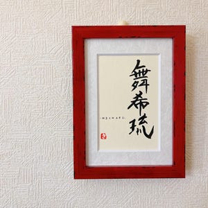 Puede incluir: Un marco de madera rojo con un paspartú blanco y una pieza de caligrafía negra en el interior. La caligrafía está en japonés y dice "Michael".