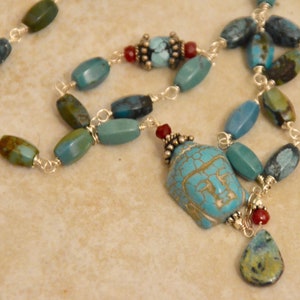 Peut inclure: Un collier de perles turquoise avec une chaîne argentée. Le collier présente un pendentif Bouddha turquoise et un charm en forme de goutte d'eau turquoise. Les perles sont de différentes nuances de bleu, vert et marron.