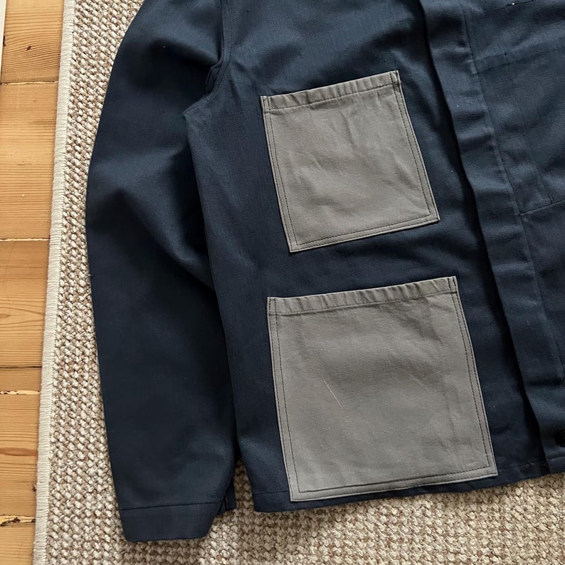 Puede incluir: Chaqueta azul marino con dos bolsillos cuadrados grises grandes. La chaqueta tiene un dise&ntilde;o cl&aacute;sico con cierre de botones y mangas largas. Los bolsillos contrastantes a&ntilde;aden un detalle &uacute;nico. Fabricada con tejido duradero.