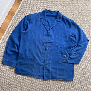 May include: A vintage cobalt blue work jacket with a collared neckline, button-up front, and two large front pockets. The jacket has long sleeves with buttoned cuffs and shows signs of wear.