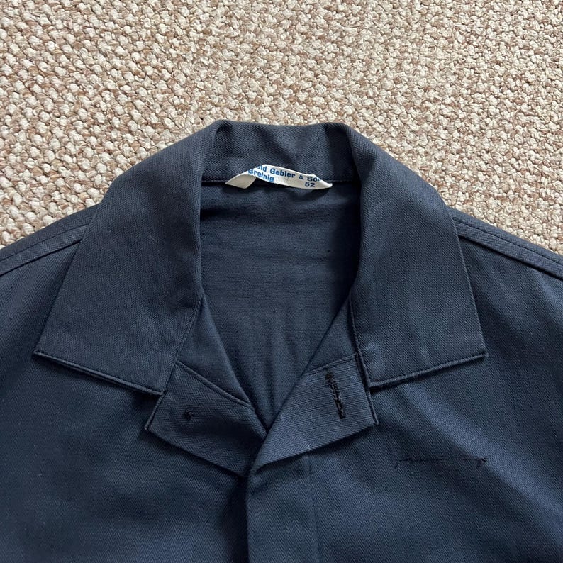 Puede incluir: Primer plano de una camisa de trabajo azul marino con cuello y cierre de botones. La camisa tiene una etiqueta en el cuello con el texto "David Gabler & Co. Drehtig". La tela parece ser un material tejido duradero.