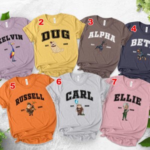 May include: A collection of seven short-sleeved t-shirts in various colors, each featuring a name in a collegiate font with a corresponding cartoon character and the text "EST. 2009". The shirts are in shades of purple, yellow, brown, navy, orange, gray, and pink.