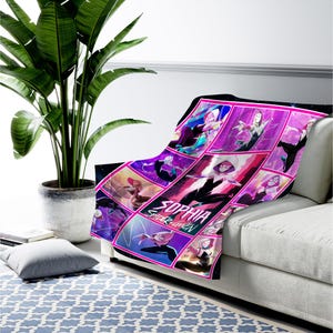 May include: A plush blanket featuring a comic book style design with the text "SOPHIA SPIDER GWEN". The blanket showcases a collage of Spider-Gwen illustrations in shades of pink, purple, and black, draped over a white sofa.