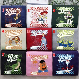 Pode incluir: Nove camisolas coloridas com personagens do filme de anima&ccedil;&atilde;o Toy Story. Cada camisola tem um design de personagem diferente, incluindo Woody, Jessie, Buzz, Slinky, Bo Peep, Aliens, Rex, Mr. Potato Head e Forky, com o ano de 1995.