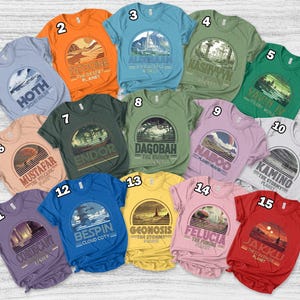 May include: A collection of fifteen short-sleeved t-shirts in various colors, each featuring a circular graphic design with text. The designs include planets and locations from a science fiction universe. The shirts are in shades of blue, orange, green, and pink.