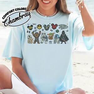 Puede incluir: Camiseta azul claro con un gr&aacute;fico de Star Wars. El dise&ntilde;o incluye personajes como Chewbacca, Stormtrooper y Darth Vader. El texto en la camiseta dice "REBEL SCUM" y "THE FORCE WITH US". La camiseta est&aacute; etiquetada como "COMFORT COLORS Chambray".