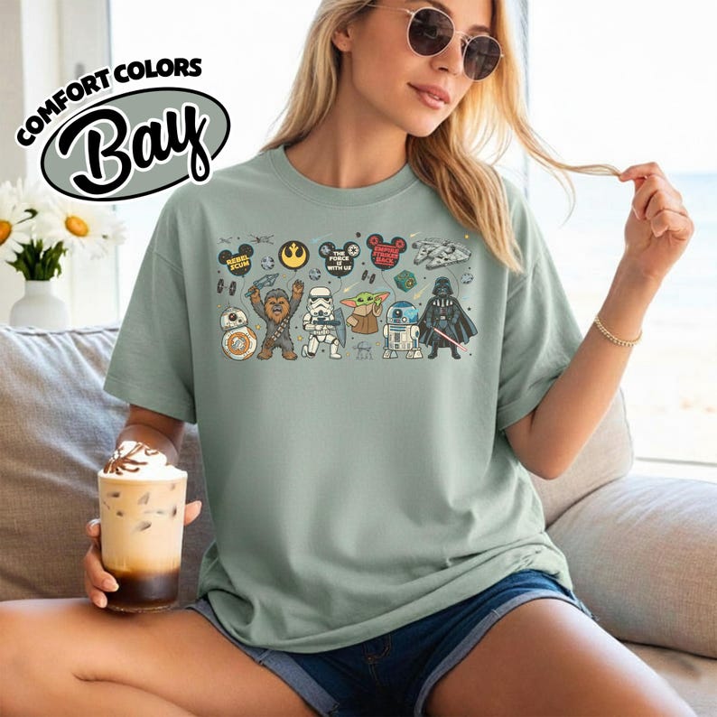 Puede incluir: Camiseta verde salvia con un gr&aacute;fico de personajes de Star Wars y orejas de Mickey Mouse. La camiseta incluye el texto "Rebel Tour" y "The Force is with Us". La camiseta est&aacute; hecha de material Comfort Colors.