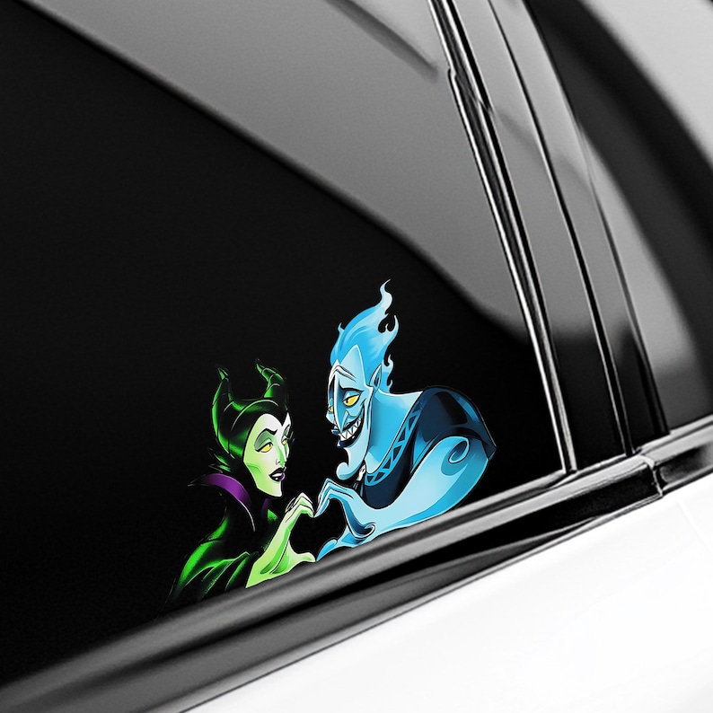 May include: A car window decal featuring a cartoon image of Maleficent and Hades forming a heart shape with their hands. Maleficent is in green and black, and Hades is blue. The decal is set against a black background.