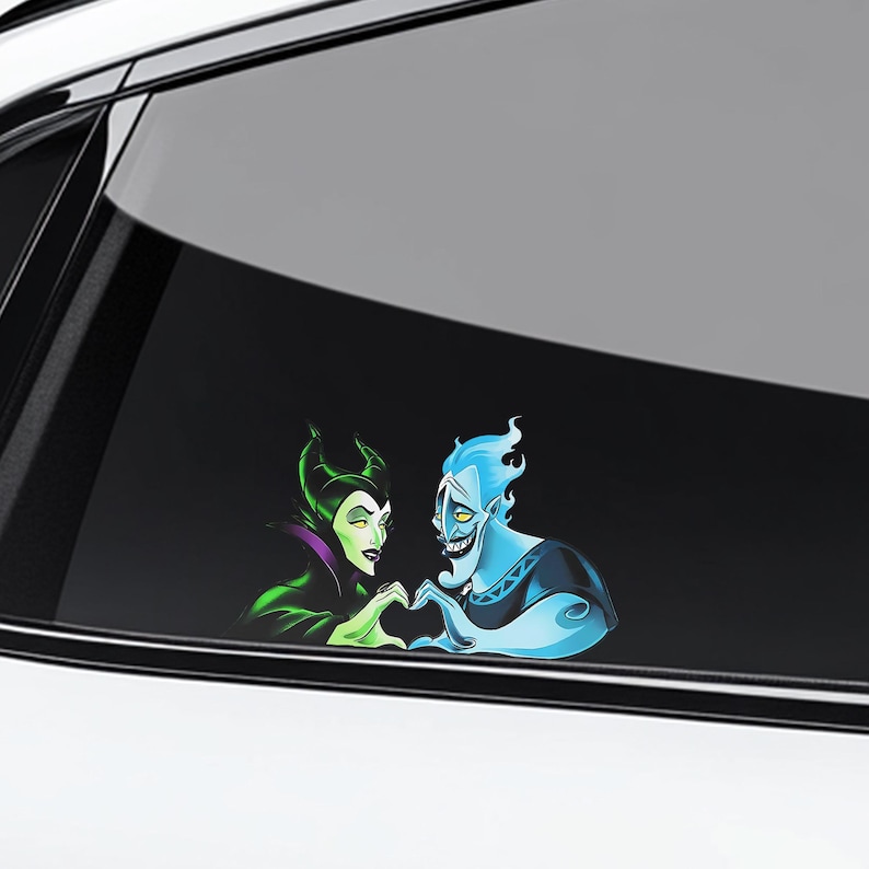 May include: A car window decal featuring cartoon characters Maleficent and Hades forming a heart shape with their hands. Maleficent is in green and purple, and Hades is blue. The decal is on a car window.