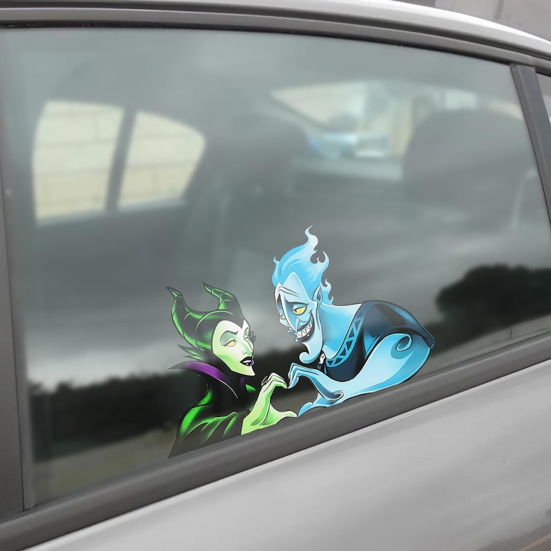 May include: A car window decal featuring cartoon characters Maleficent and Hades forming a heart shape with their hands. Maleficent is in a black and green outfit, and Hades is blue with flame-like hair. The decal is applied to a car window.