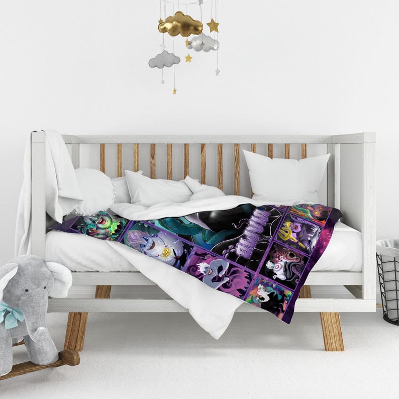 Op de afbeelding: Een kleurrijke babydeken met een collage van stripfiguren in een rasterpatroon. De deken is over een witte wieg met wit beddengoed gedrapeerd. De figuren zijn in tinten groen, paars en zwart.