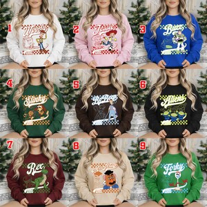 Pode incluir: Nove camisolas de gola redonda com personagens de um filme de anima&ccedil;&atilde;o popular. As camisolas s&atilde;o em v&aacute;rias cores, incluindo branco, rosa, azul, verde, castanho, preto e bord&ocirc;. Cada camisola tem um gr&aacute;fico de personagem e o ano "1995" impresso.