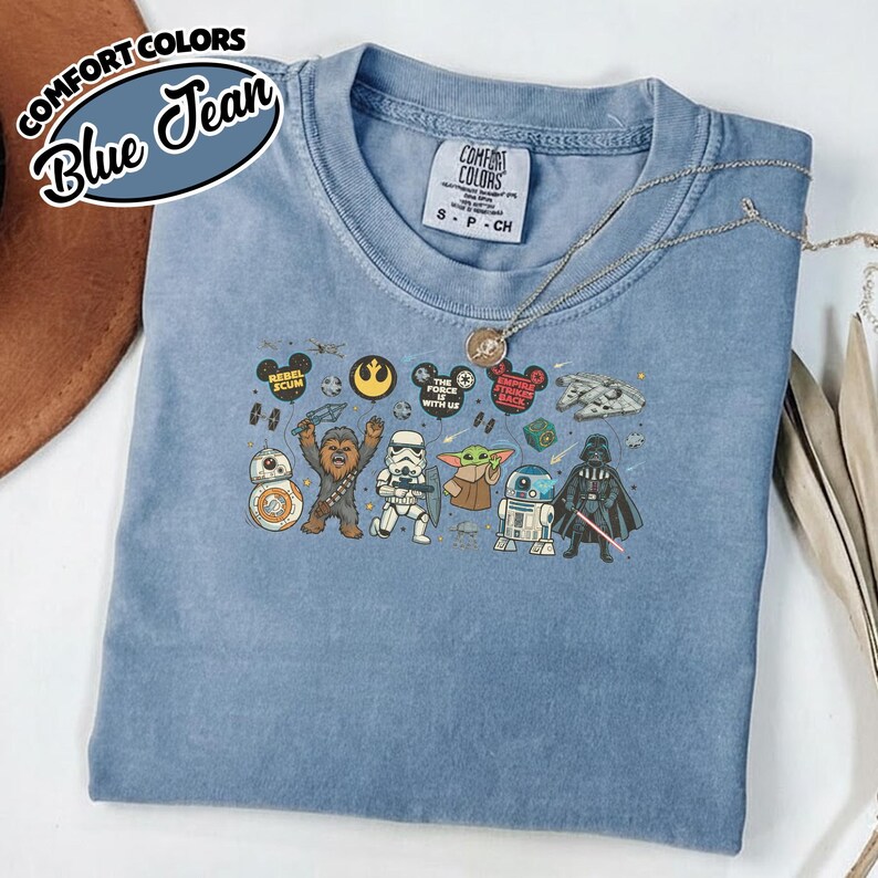 Puede incluir: Camiseta azul vaquero con personajes y frases de Star Wars. La camiseta incluye im&aacute;genes de BB-8, Chewbacca, un Stormtrooper, Grogu, R2-D2 y Darth Vader. La camiseta tambi&eacute;n tiene las palabras "Comfort Colors" y "Blue Jean" impresas.