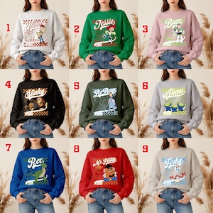 Pode incluir: Uma cole&ccedil;&atilde;o de nove camisolas de gola redonda com v&aacute;rios personagens de um filme de anima&ccedil;&atilde;o popular. Cada camisola exibe o nome e a imagem de um personagem, juntamente com o ano de 1995. As camisolas est&atilde;o dispon&iacute;veis em uma variedade de cores.