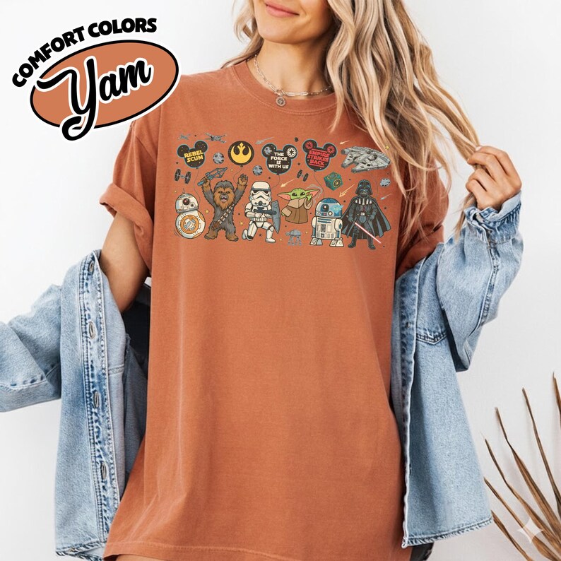 Puede incluir: Una camiseta de color &oacute;xido con un dise&ntilde;o de Star Wars. El dise&ntilde;o incluye personajes como BB-8, Chewbacca, Stormtrooper, Yoda, R2-D2 y Darth Vader. La camiseta tambi&eacute;n tiene el texto "COMFORT COLORS" y "Yam".