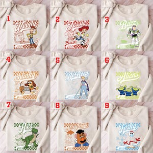 Pode incluir: Uma cole&ccedil;&atilde;o de nove camisolas bege, cada uma com um personagem diferente do filme de anima&ccedil;&atilde;o "Toy Story". Os designs incluem Woody, Jessie, Buzz, Slinky, Bo Peep, Aliens, Rex, Mr. Potato Head e Forky, com o ano "1995".