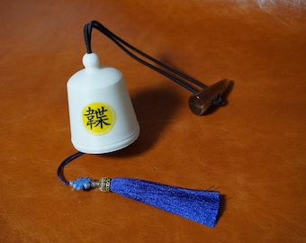 Könnte beinhalten: Weiße Keramikglocke mit einem schwarzen Quasten und einem gelben Kreis mit schwarzen Kanji-Zeichen, die "快樂" lesen. Die Glocke hängt an einer schwarzen Schnur mit einem braunen Holzclip.