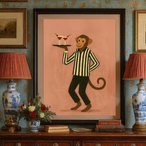 May include: A framed wall art print featuring a cartoon monkey wearing a black and white striped shirt and dark pants, holding a black tray with two cocktail glasses garnished with red cherries against a solid light peach background.