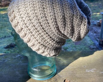 May include: A beige crocheted beanie hat with a slouchy fit. The hat is made with a textured stitch pattern and has a subtle ombre effect.