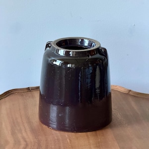 May include: A dark brown, cylindrical ceramic crock with a glossy, reflective glaze. The vessel features a wide, open top with a thick, reinforced rim and two small, integrated lug handles positioned symmetrically on the upper sides of the body.