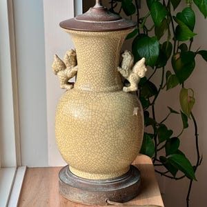 May include: A vintage table lamp with a crackle glaze finish in shades of yellow and brown. The lamp features two small, winged figures and a metal base. The lamp is approximately 24 inches tall.