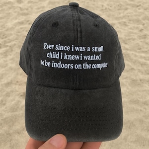 Può includere: Un cappellino da baseball nero con testo ricamato bianco. Il testo recita: "Da quando ero bambino sapevo che volevo stare al chiuso sul computer". Il cappellino è realizzato in un materiale morbido e usurato.