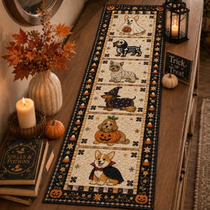 May include: A rectangular quilted table runner featuring a series of six square panels, each depicting a dog in a different Halloween costume, including a ghost, skeleton, mummy, witch, pumpkin, and vampire, bordered by a black candy corn pattern.