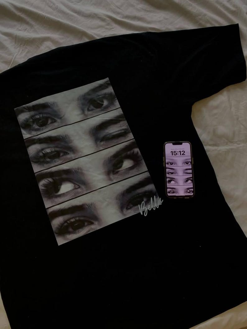 Puede incluir: Camiseta negra con un gr&aacute;fico de cinco ojos en fila, cada uno con una expresi&oacute;n diferente. El texto "Bella" est&aacute; escrito en blanco en la esquina inferior derecha del gr&aacute;fico.